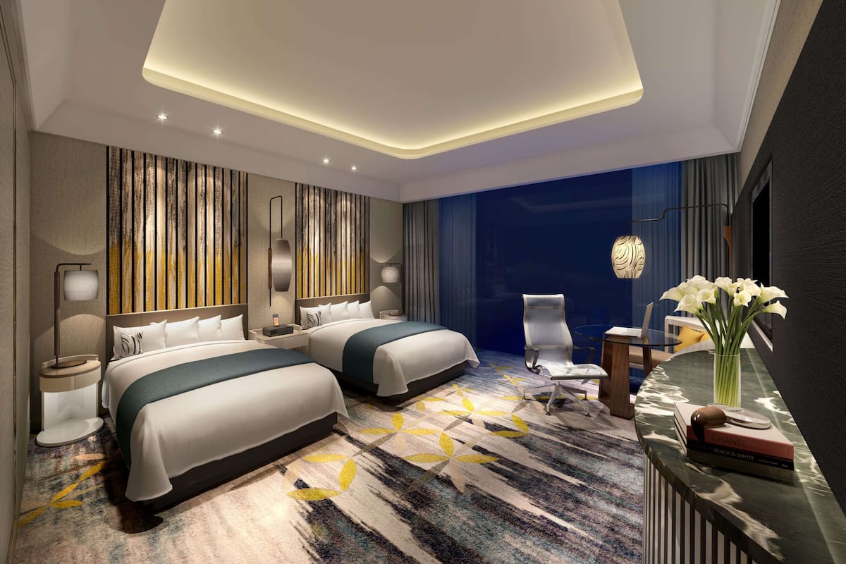 Une chambre d’hôtel moderne avec deux lits, un bureau, une chaise et une grande fenêtre.