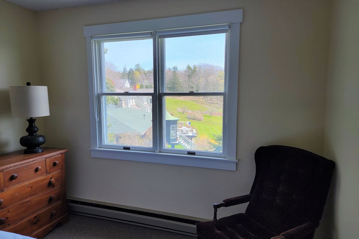 A room with a large window, a wooden dresser, and a dark chair.