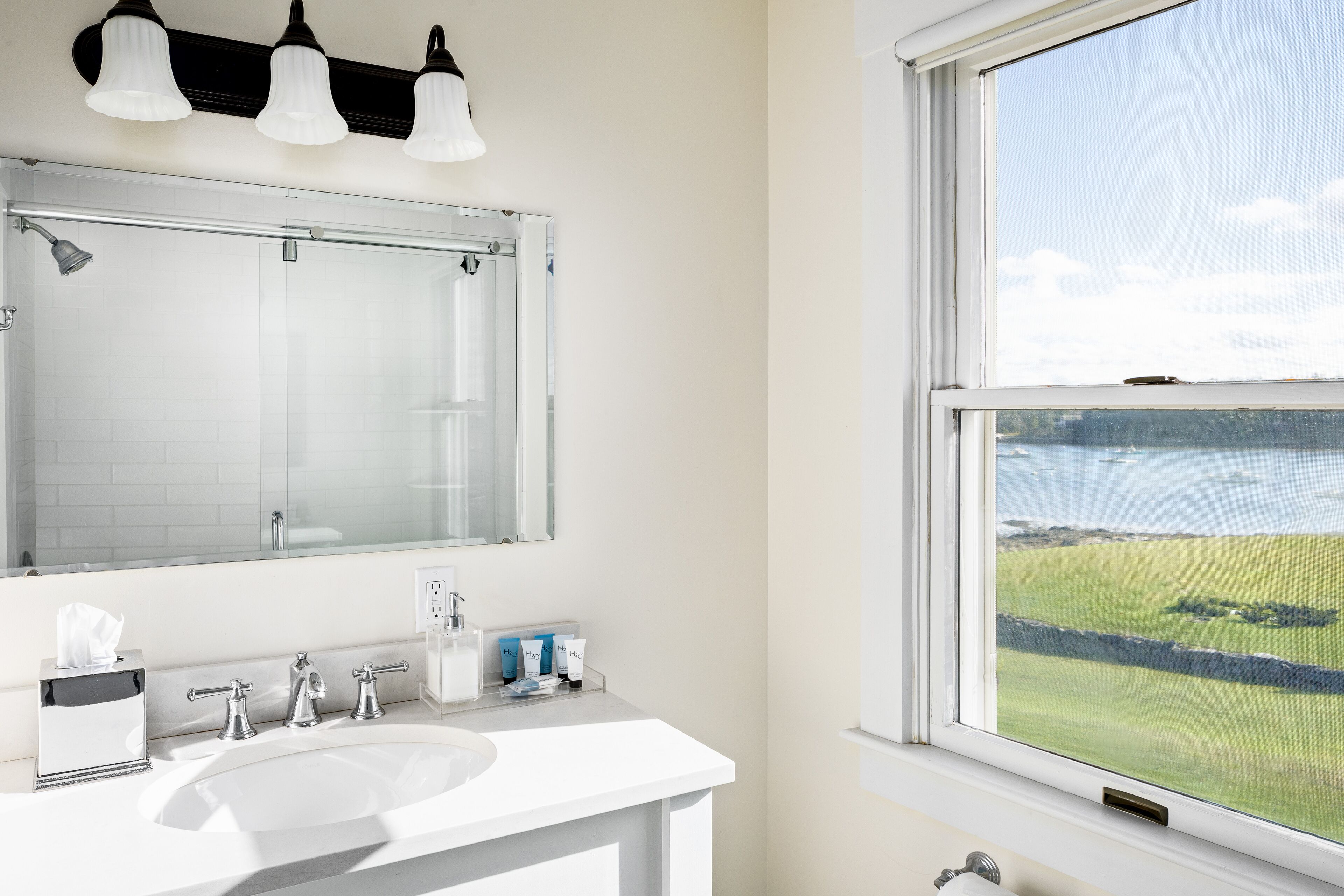 A bathroom with a large mirror, a sink, and a window offering a view of the sea.