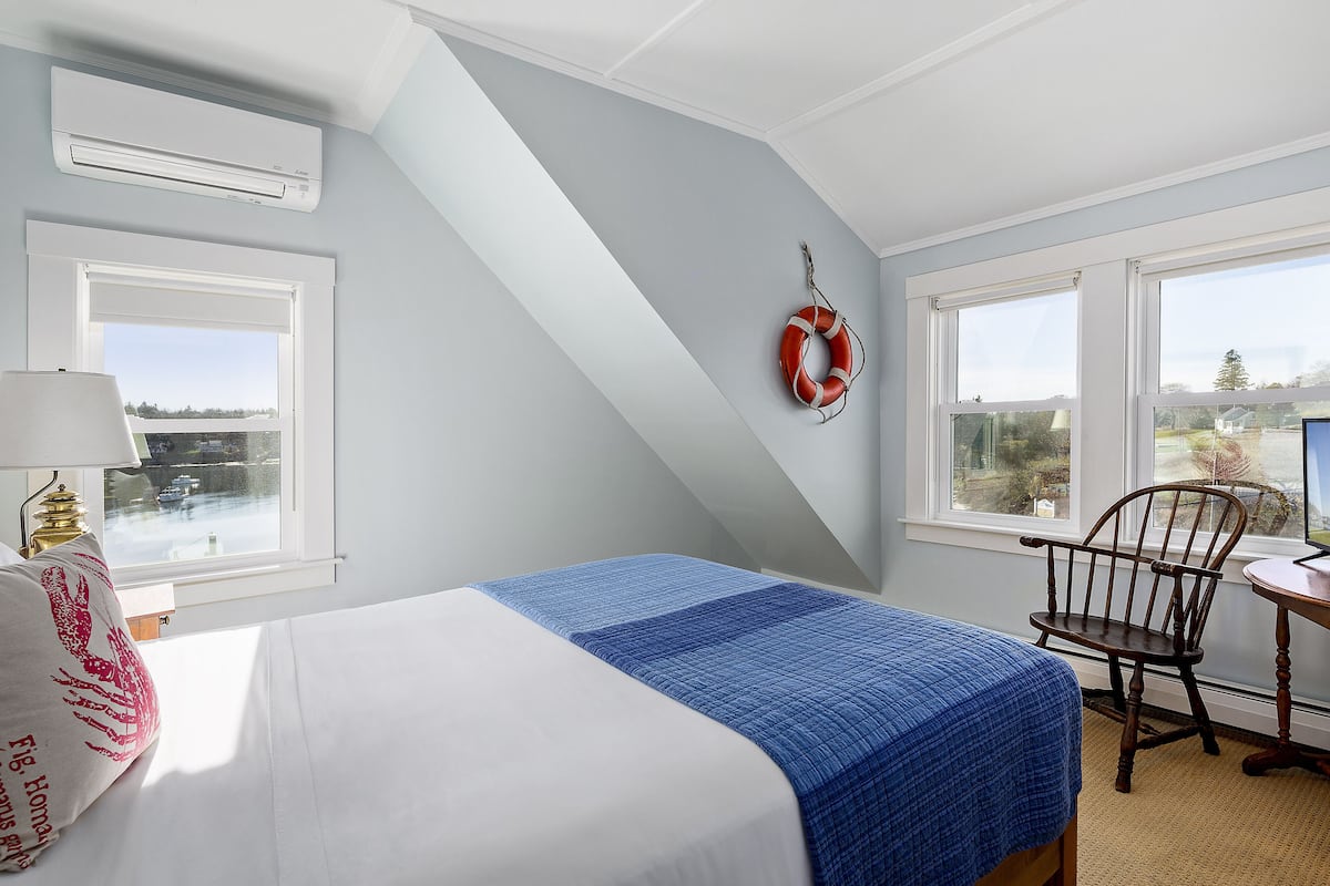 A bedroom with a bed, a chair, a desk, and a window with a view.