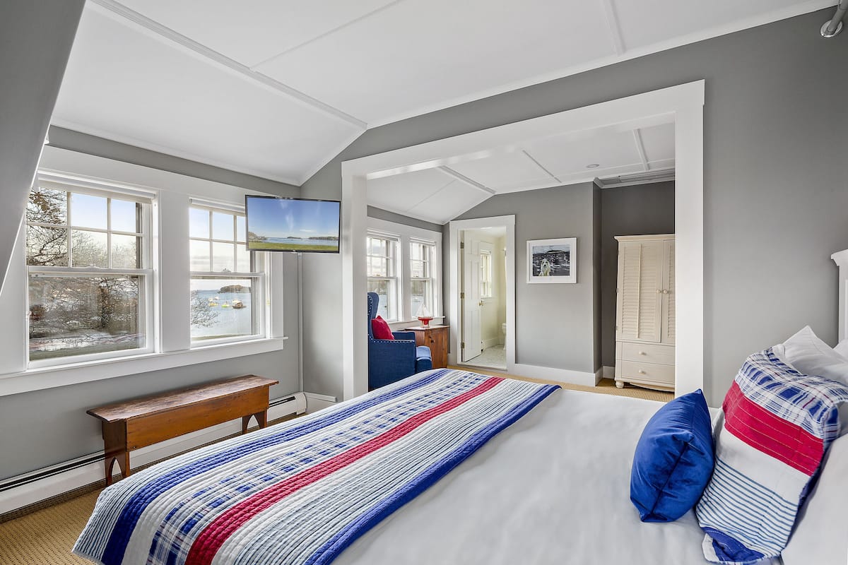 A bedroom with a large bed, a bench, a TV, and a view of the outdoors.