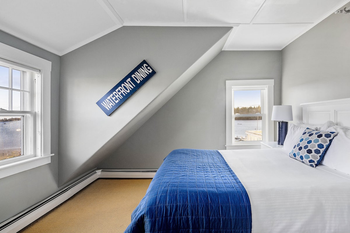 A bedroom with a bed, a window, a waterfront dining sign, and a view of the water.