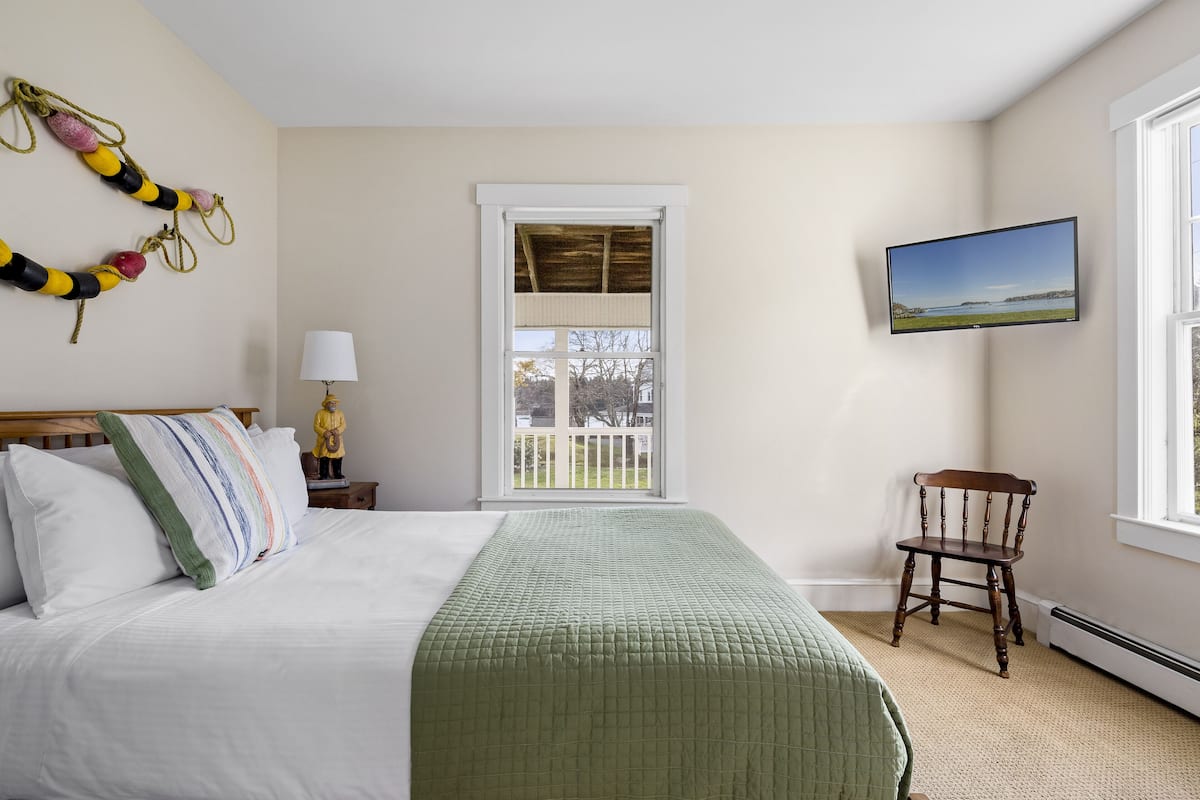 A bedroom with a bed, a chair, a TV, a window, and a view of the outdoors.