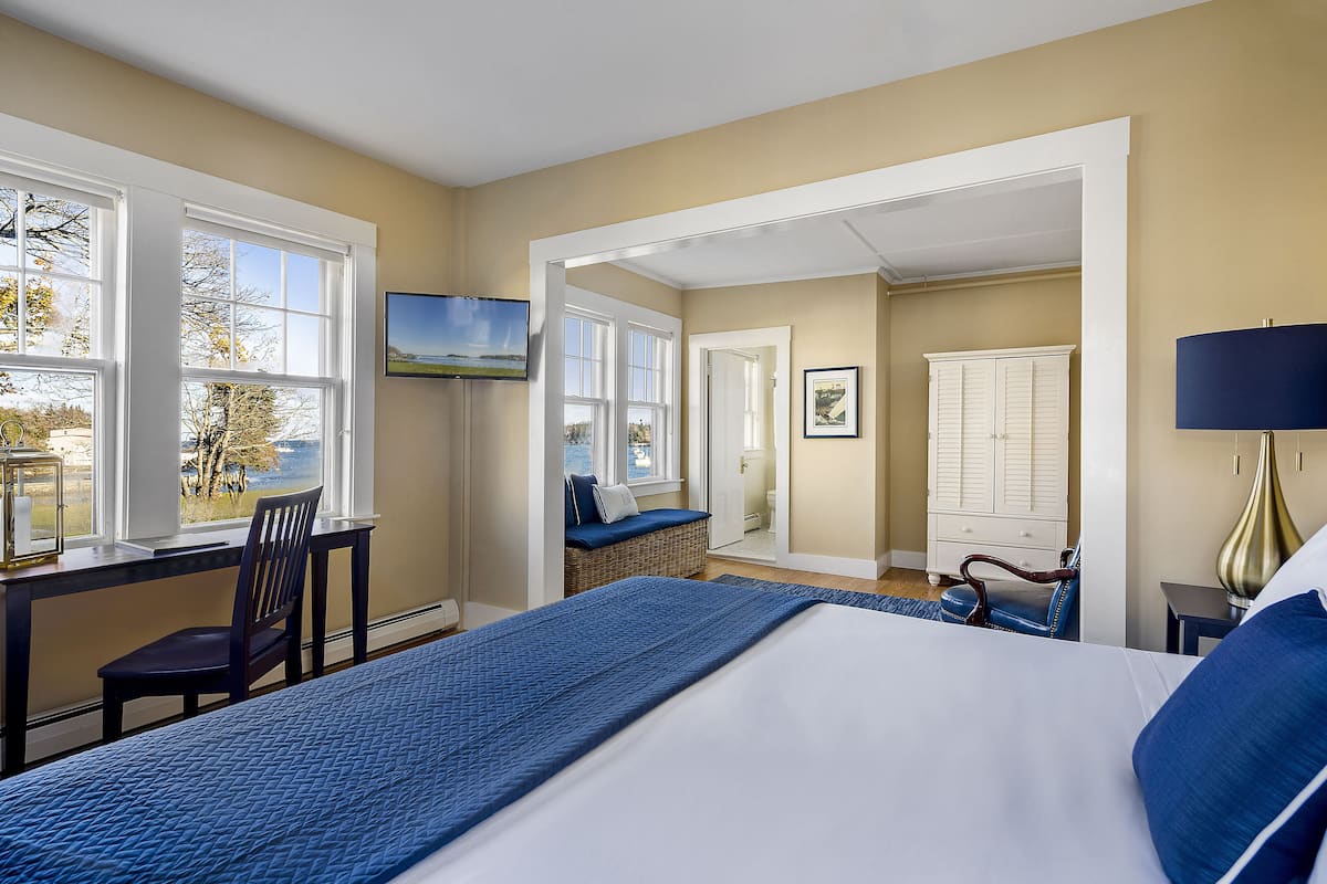 A bedroom with a large bed, a desk, and a chair. There is a window with a view of trees and a building.