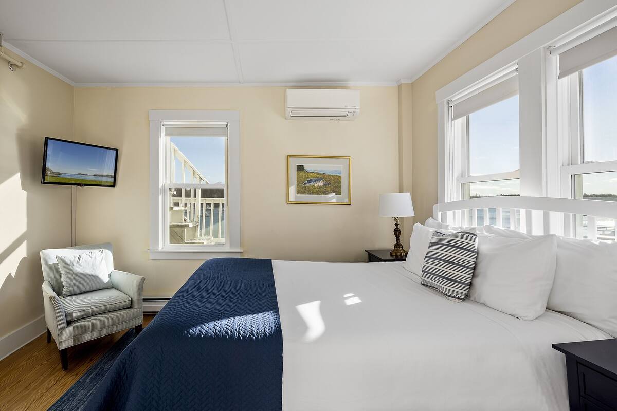 A hotel room with a large bed, a chair, a TV, and a window with a view.