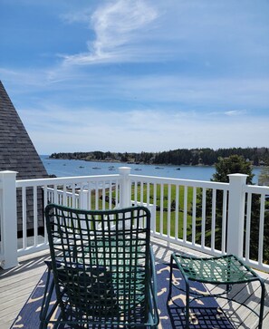 A deck with a view of a lake, featuring two green chairs and a small table. - East Wind Inn on the Water (Tenants Harbor)