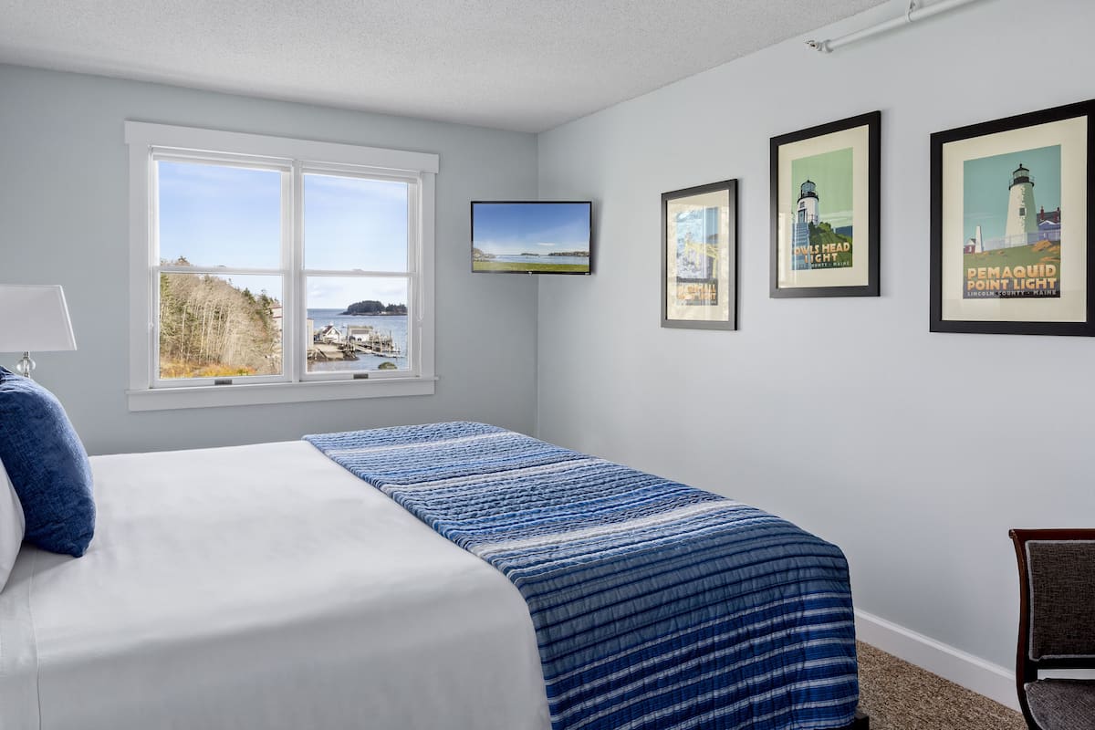 A bedroom with a bed, a window with a view, and two framed pictures on the wall.