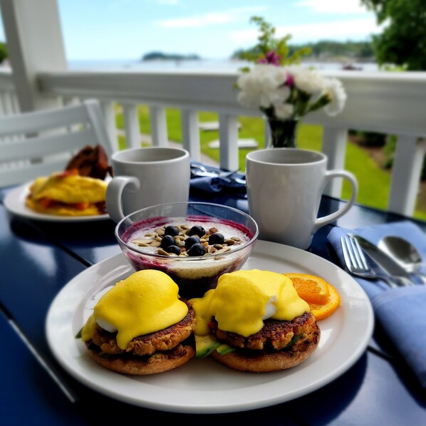 A breakfast setup with eggs benedict, a bowl of yogurt with berries, and two coffee cups on a table. - East Wind Inn on the Water (Tenants Harbor)