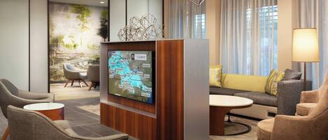 A modern lobby with a large flat-screen TV displaying a map, comfortable seating, and a chandelier.