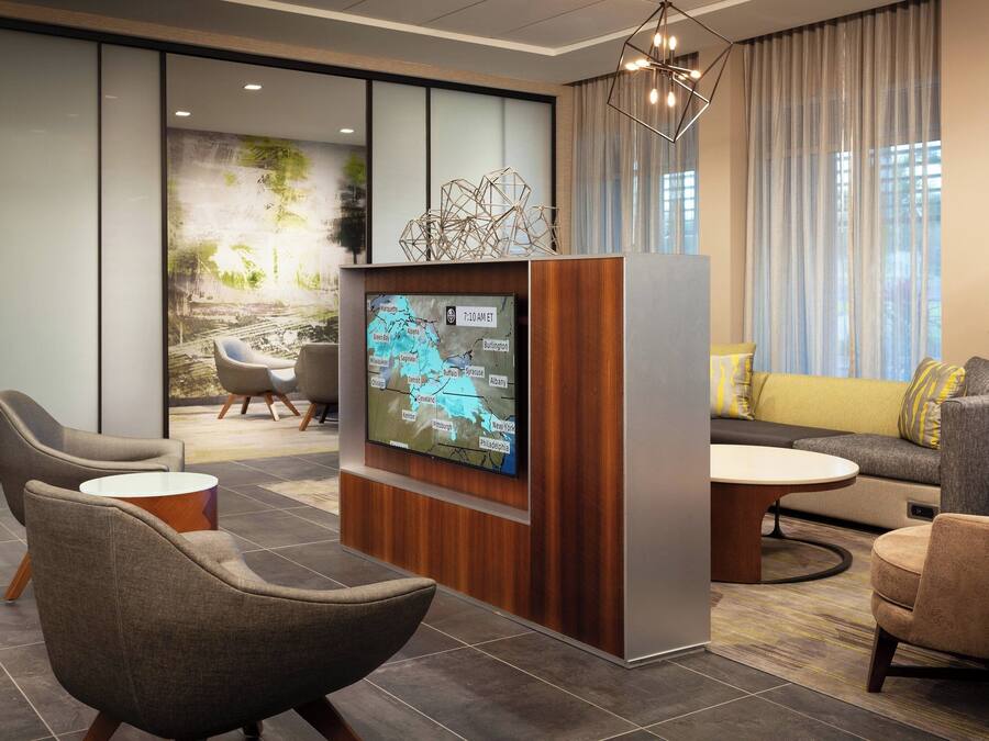 A modern lobby with a large flat-screen TV displaying a map, comfortable seating, and a chandelier.