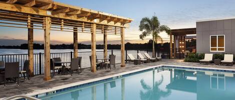 Un área de piscina con una pérgola de madera, sillones de descanso y vistas al agua.