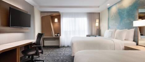 A hotel room with a desk, two beds, a flat-screen TV, a desk lamp, and a large window with curtains.