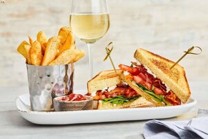 A plate with a grilled sandwich, a glass of white wine, and a container of fries.