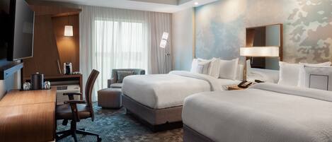 A hotel room with two beds, a desk with a computer, a TV, and a large mirror.
