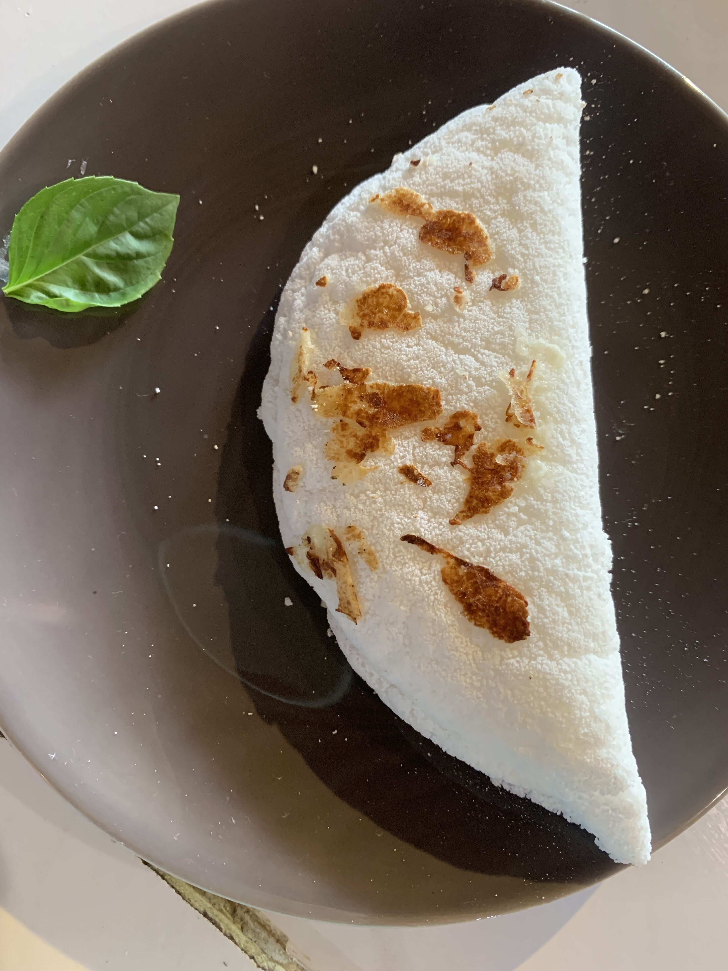 A triangular crepe on a dark plate with a green leaf garnish.