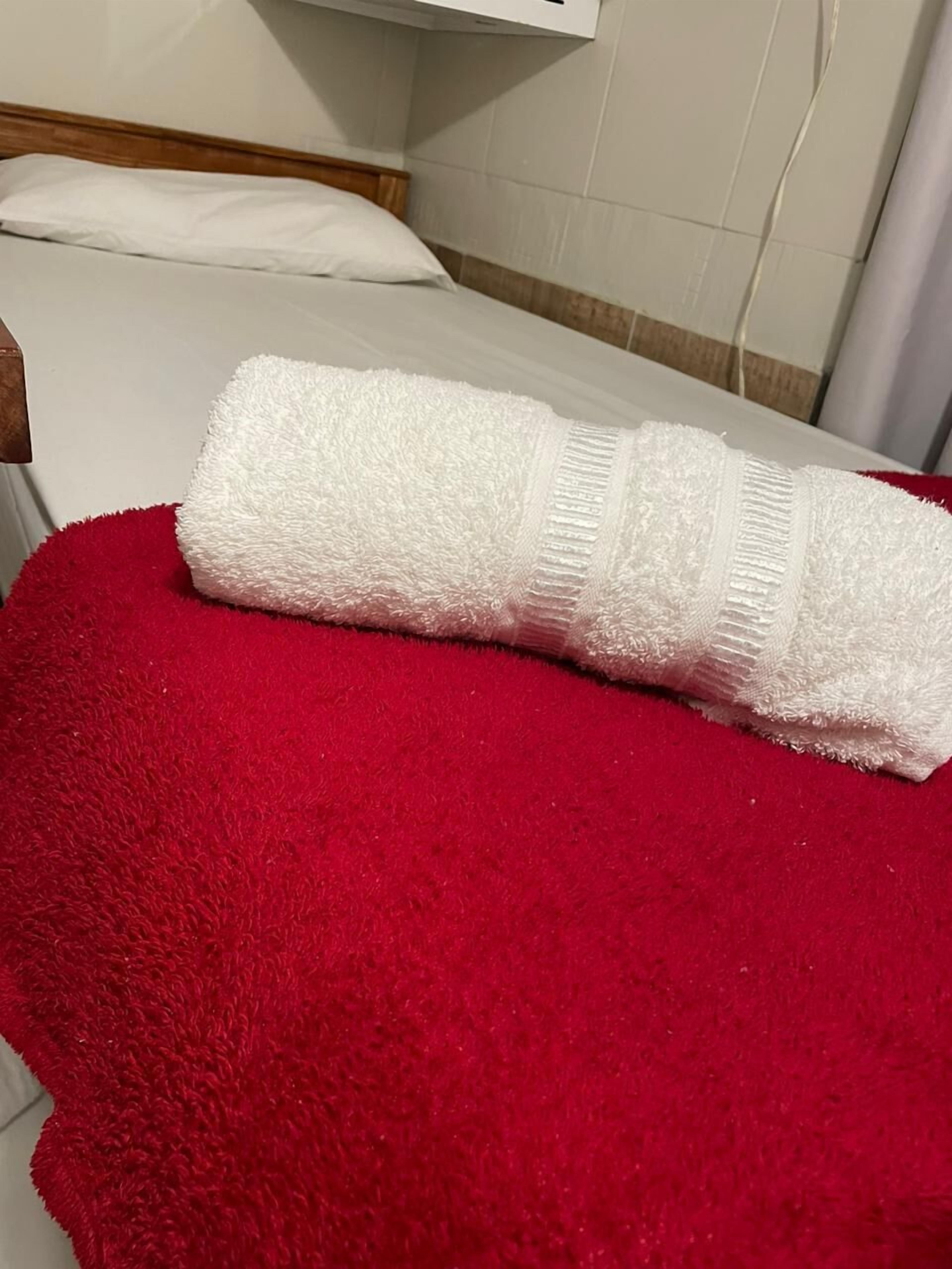 A neatly made bed with white linens and a red bath mat.