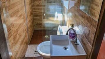 Un baño compacto con paneles de madera, mampara de ducha de vidrio, lavamanos y espejo.