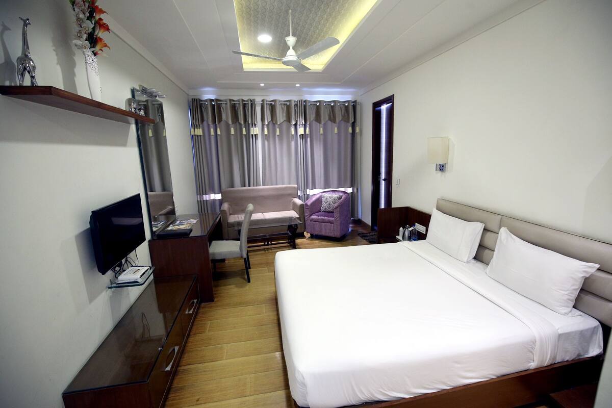 A hotel room with a bed, a TV, a desk, a chair, and a ceiling fan.