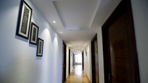 A long, narrow hallway with wooden floors and white walls. There are several framed pictures on the walls and doors leading to rooms. - Royal Inn (Muktsar)