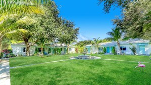A well-maintained lawn with a central fountain, surrounded by palm trees and a row of light blue buildings with a uniform architectural style. - Cottages El Portal (Miami)