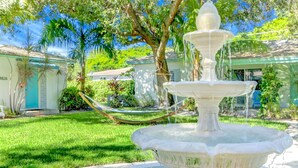 A white stone fountain with multiple tiers, surrounded by a well-maintained lawn and a hammock. - Cottages El Portal (Miami)