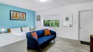 A modern bedroom with a bed, a blue sofa, and a window with a view of greenery. - Cottages El Portal (Miami)