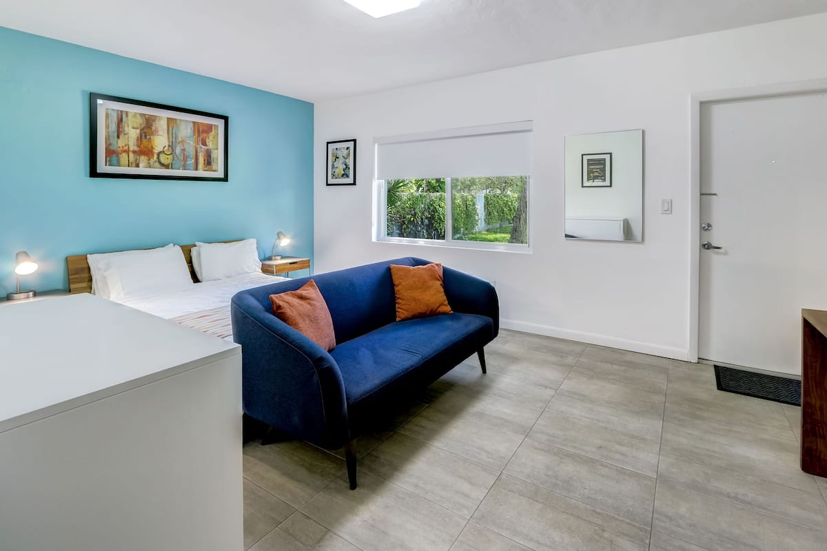 A modern bedroom with a bed, a blue sofa, and a window with a view of greenery.