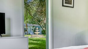 A bedroom with a bed, a TV, and a view of a garden with a fountain. - Cottages El Portal (Miami)
