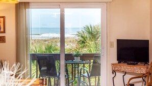 Ett rum med en TV, ett bord med stolar, utsikt över havet och en balkong med växter.