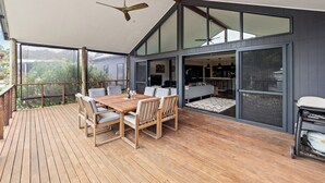 Une terrasse en bois avec une table et des chaises, de grandes fenêtres et un ventilateur de plafond.