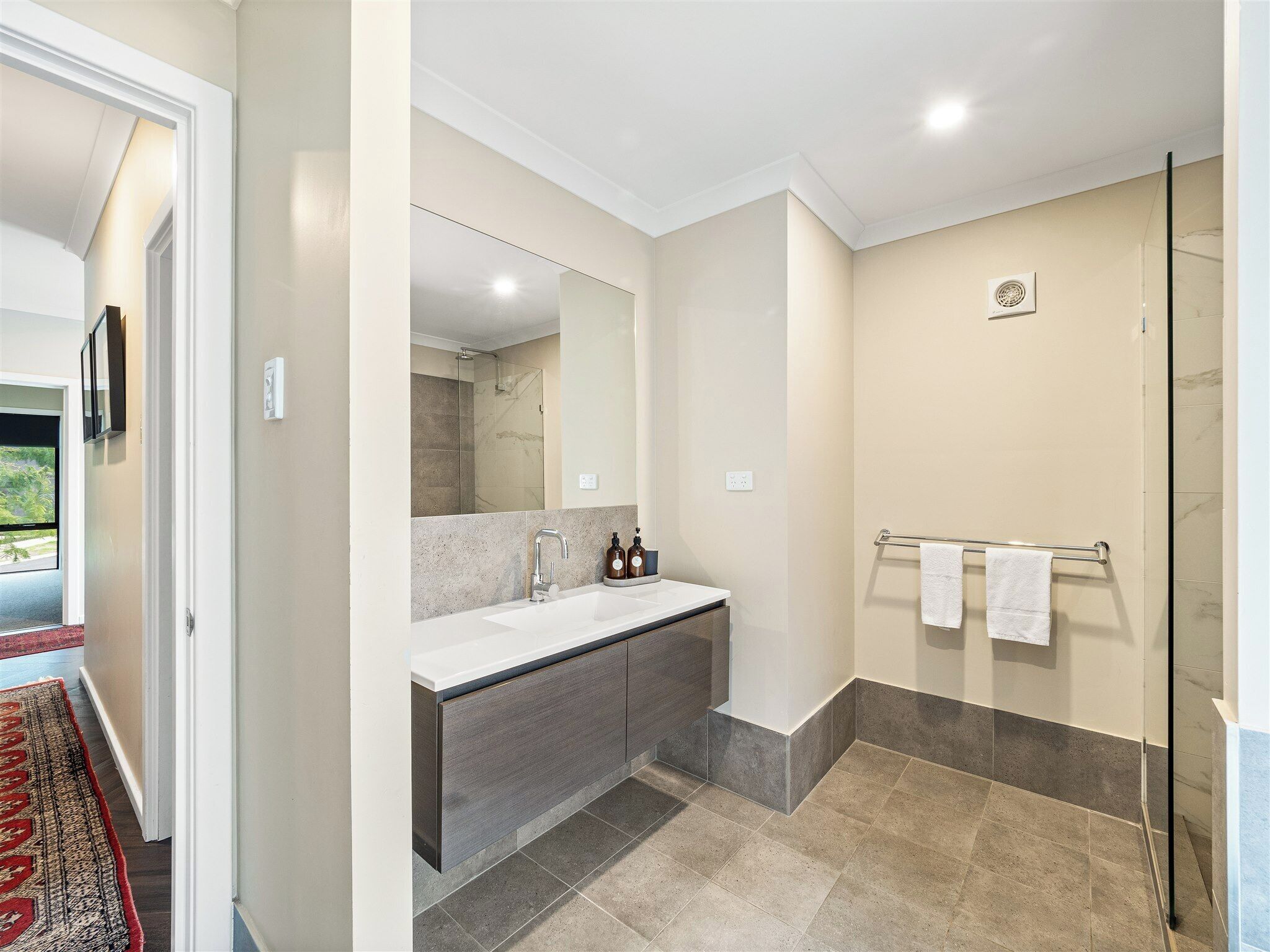 Un baño moderno con cabina de ducha de vidrio, un espejo grande y un mueble de tocador con lavabo y espacio de almacenamiento.