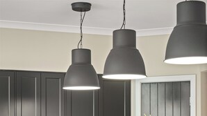 Une cuisine moderne avec des meubles de couleur sombre, un îlot central doté de tabourets, un four à micro-ondes, un four traditionnel et un vase rempli de fleurs.