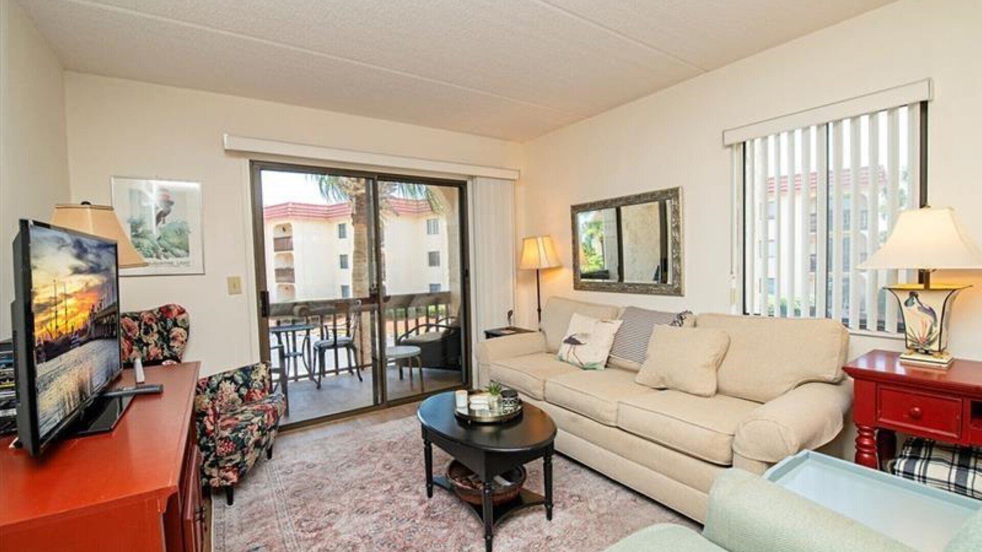 Un salon avec un canapé, une table basse et un téléviseur posé sur un meuble. Il y a un balcon d’où l’on peut admirer la vue sur les immebles, et il est doté d’une rambarde.