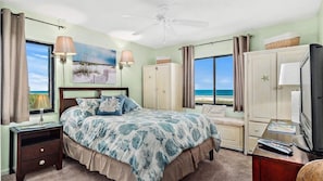 Quarto com cama, mesas de cabeceira, cômoda, televisão e vista para a praia.