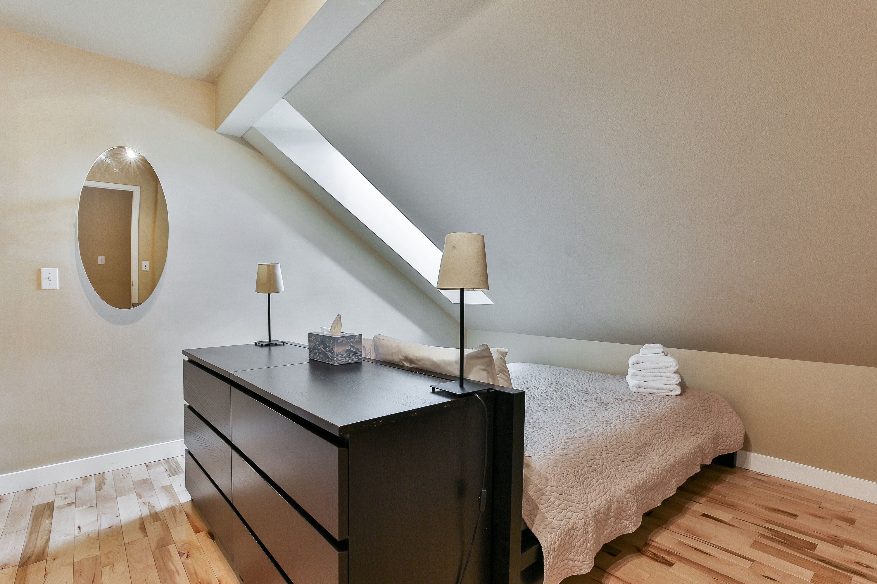 A bedroom with a bed, a dresser, a mirror, and a lamp.