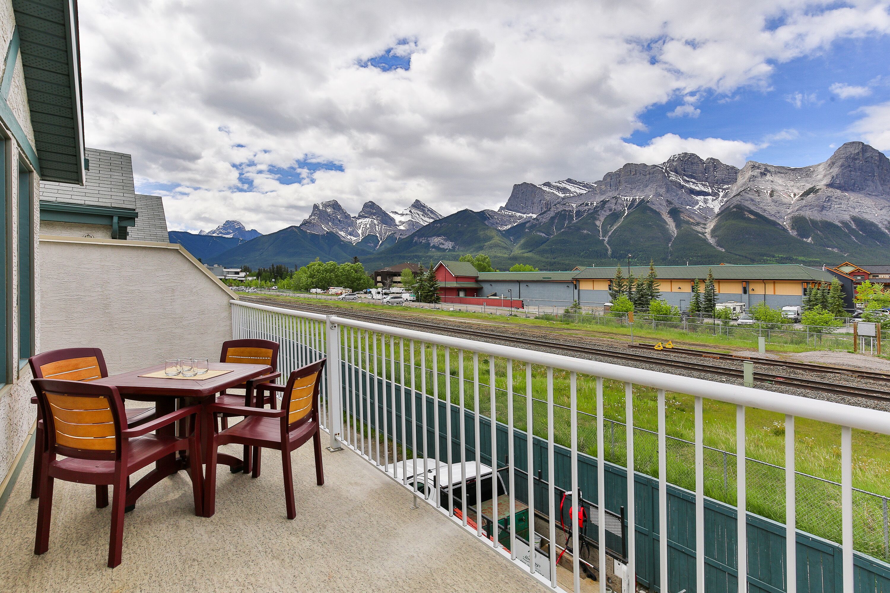 Un balcon avec une table et des chaises donnant sur une voie ferrée et des montagnes.