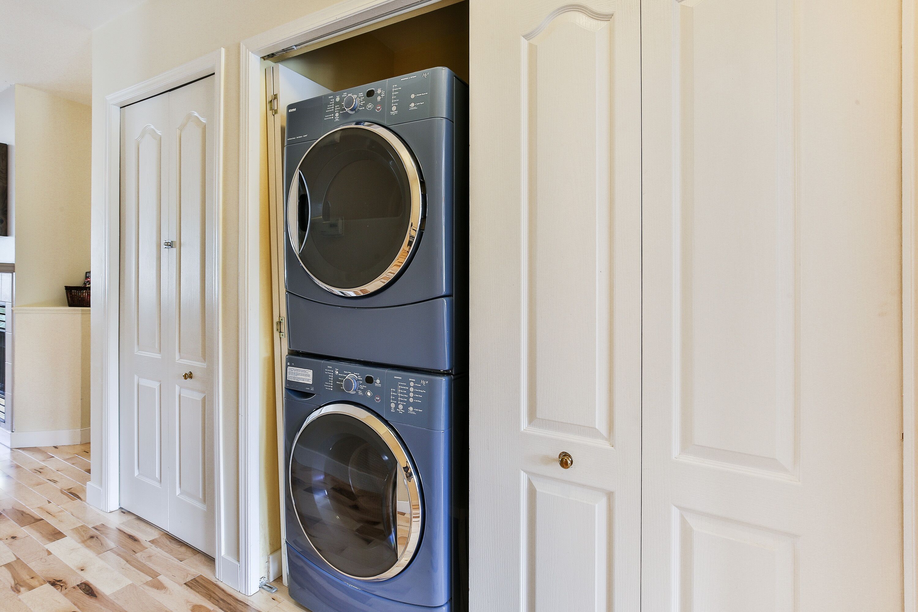 A stacked washer and dryer unit in a hallway with white doors.