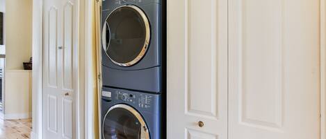 A stacked washer and dryer unit in a hallway with white doors.