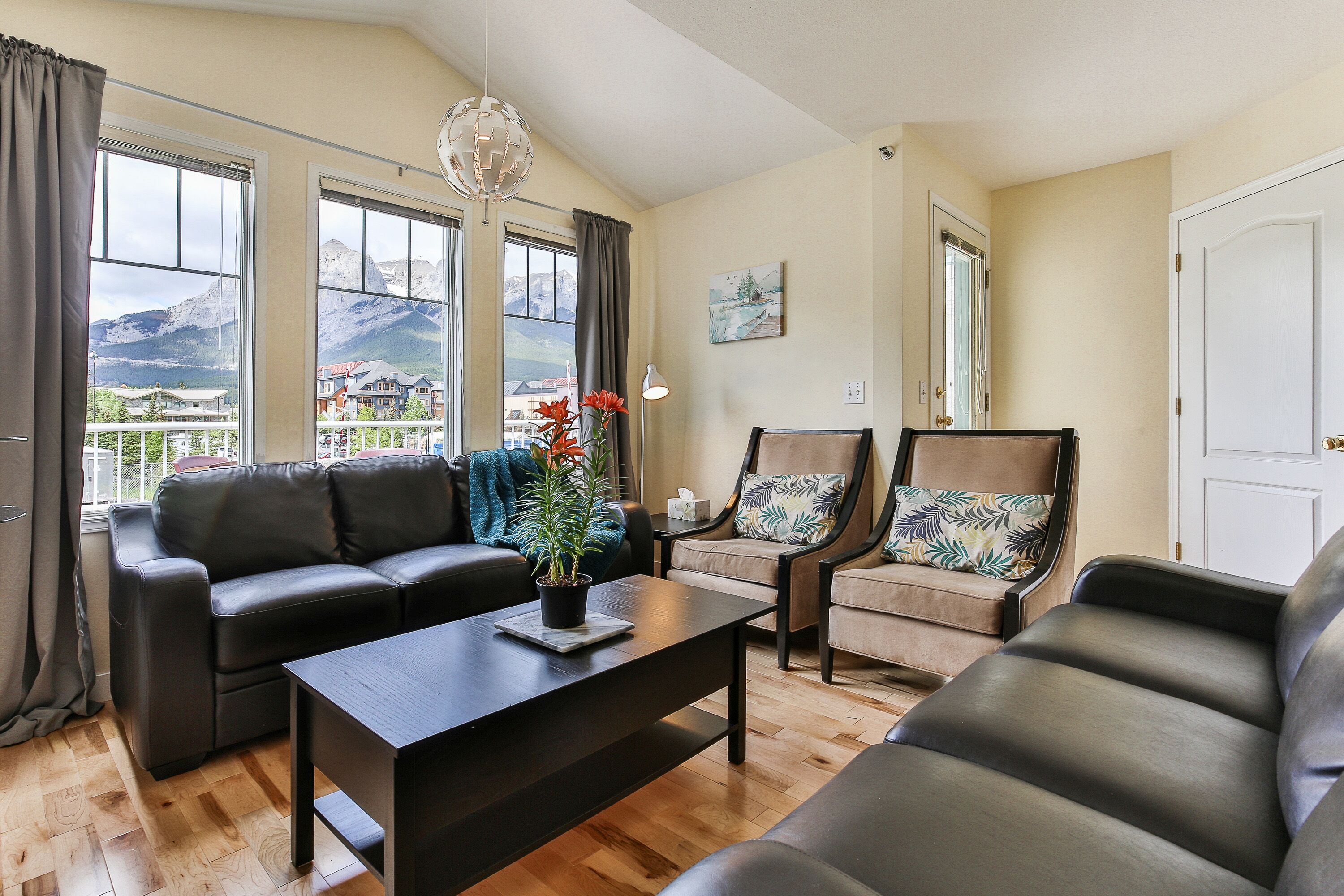 A living room with a sofa, armchairs, a coffee table, and a view of mountains through large windows.