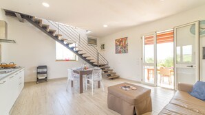 Un amplio salón con escaleras, una mesa de comedor con sillas, un sofá y una zona de cocina con encimera y armarios.