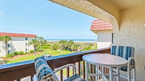 Un balcon avec vue sur la plage, une table et deux chaises.