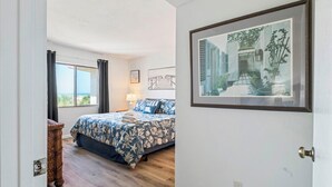Ein Schlafzimmer mit einem Bett, einer Lampe, einem gerahmten Bild und Blick ins Freie.