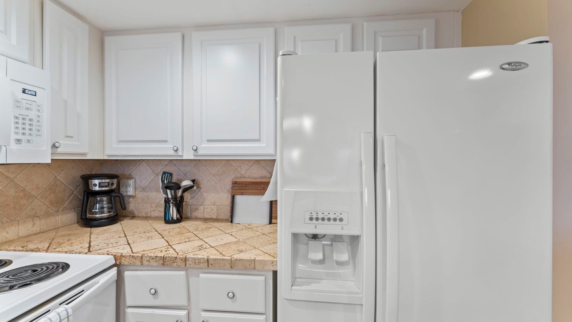 A kitchen with white cabinets, a coffee maker, a refrigerator, and a stove.