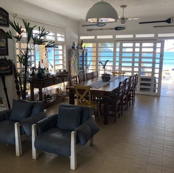 Un salón amplio con una gran mesa de comedor, asientos cómodos y vistas al océano a través de ventanas grandes.