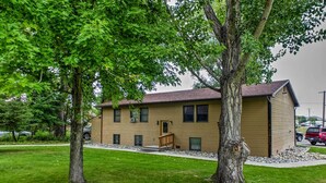 A two-story building with a flat roof, a front porch, and a small front yard with a bench. - Cozy Angler's Apt - Steps to Trout Fishing River! (Columbus)