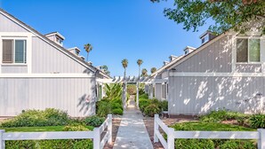A row of modern, single-story buildings with a central pathway flanked by white fences and lush greenery. - Best Deal in Carpinteria! (Carpinteria)