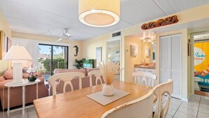 Un salón luminoso con una mesa de comedor de madera, sofás a rayas y un ventilador de techo.