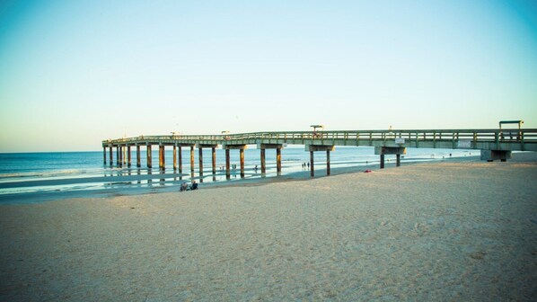 A pier extending into the ocean with a sandy beach in the foreground.