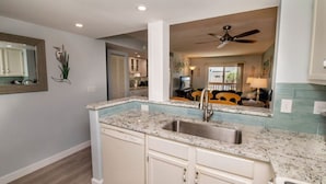 Una cocina con encimera de granito, pileta de acero inoxidable y muebles blancos.