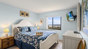 Une chambre à coucher comprenant un lit, des tables de chevet, une fenêtre avec vue et des œuvres d’art murales.